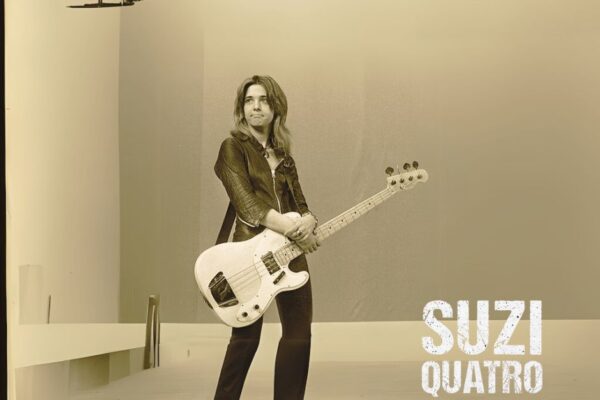Suzi Quatro performing live on stage, wearing her iconic leather outfit and playing bass guitar.